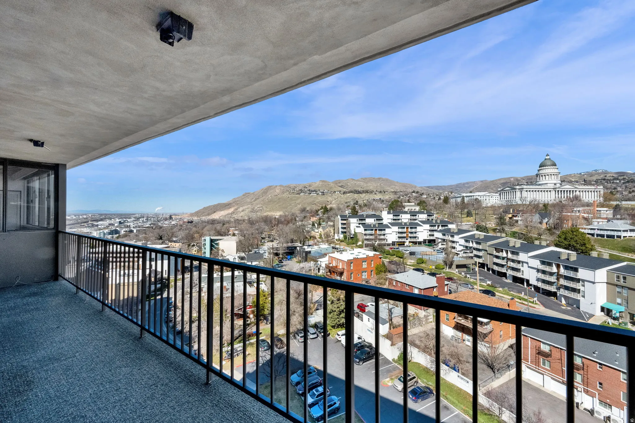 Balcony with black metal railing, concrete flooring, and an expansive skyline with distant architectural and natural elements