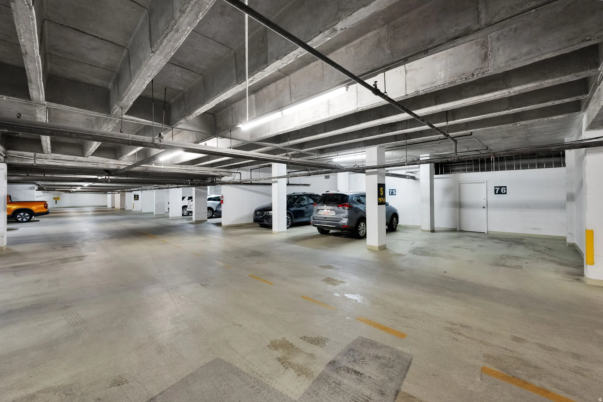 Underground parking garage featuring concrete flooring and exposed concrete ceiling beams
