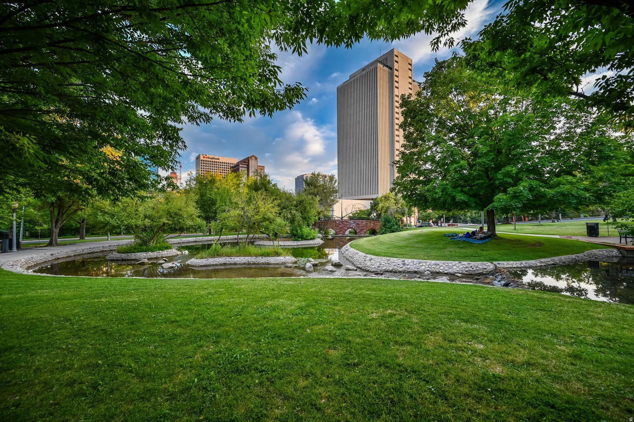 Manicured green spaces featuring mature trees and a tranquil pond with stone-lined edges