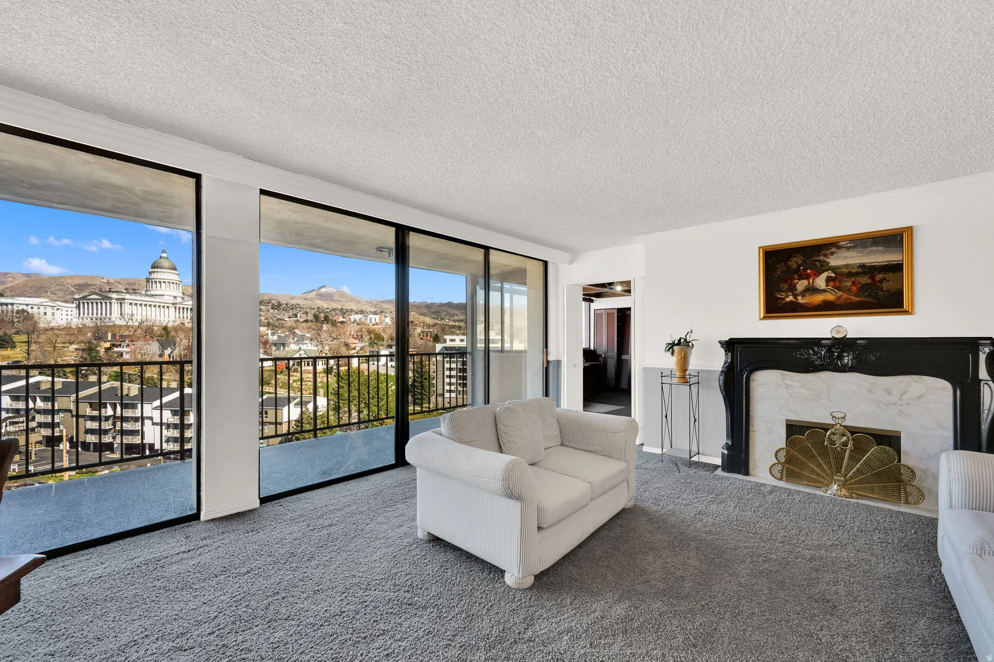 Expansive windows, balcony access, and a decorative fireplace with a marble surround and ornate black mantel
