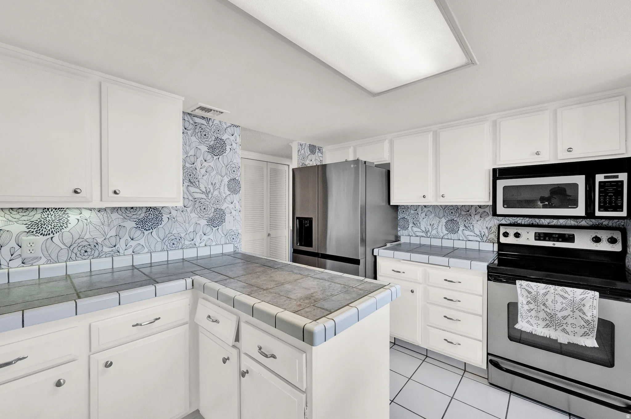White cabinetry with brushed nickel hardware, stainless steel refrigerator, built-in microwave, and tile countertops