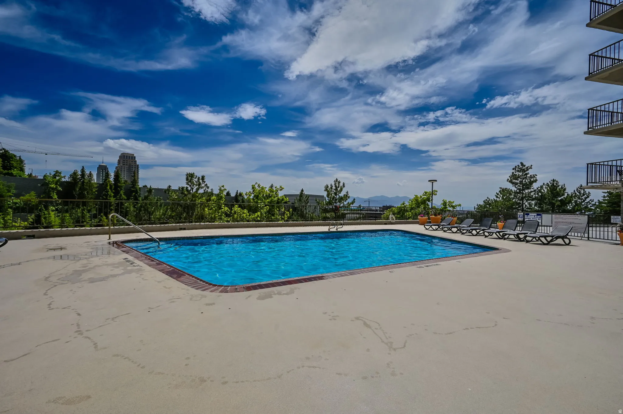 Rectangular swimming pool with a concrete surround, metal handrails, and a red brick border