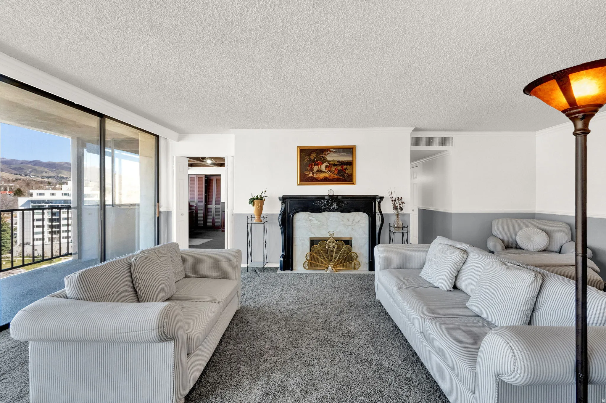 Floor-to-ceiling sliding glass doors, black metal balcony railing, black fireplace surround, white marble-finish fireplace, and grey carpet