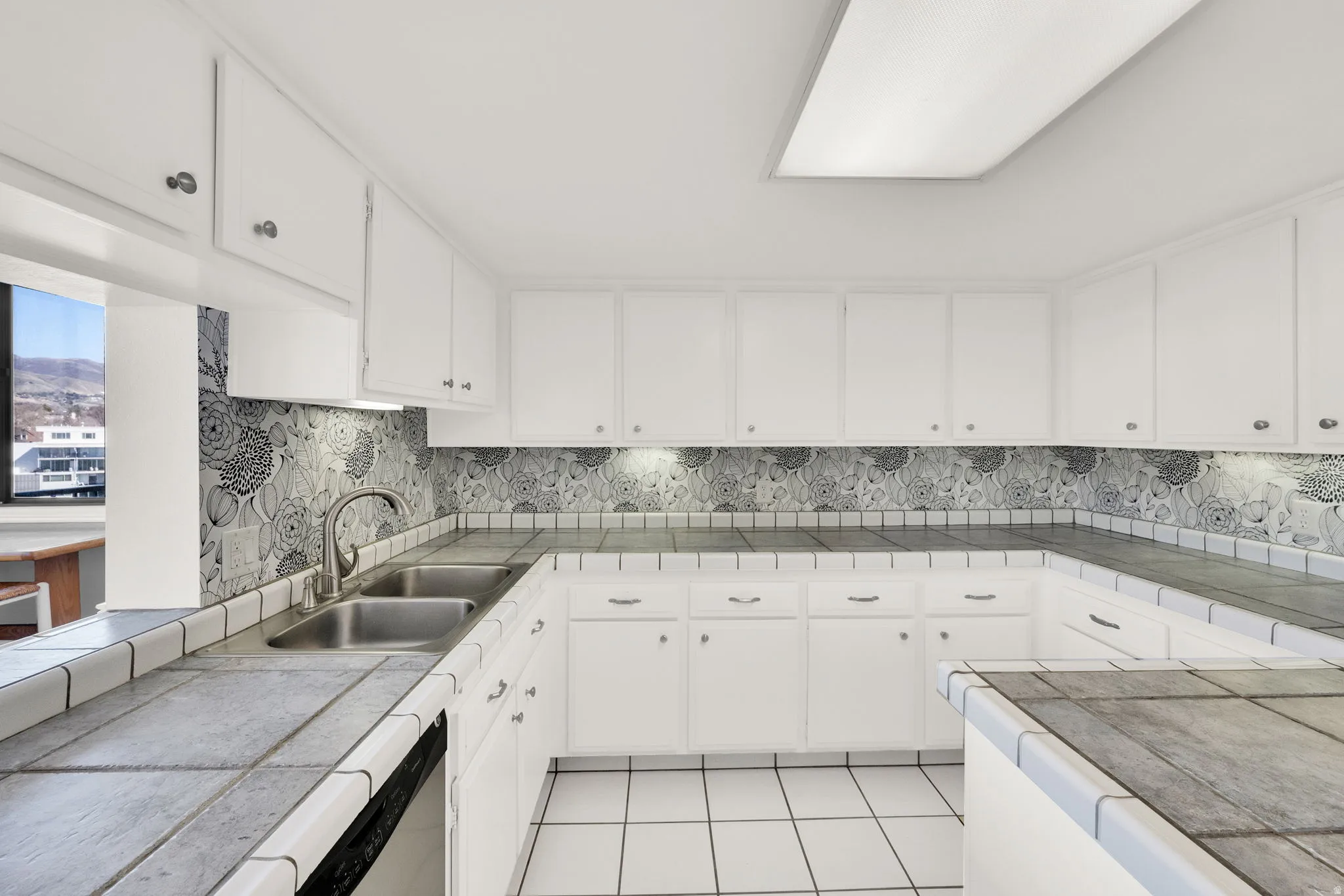 U-shaped kitchen featuring white cabinetry, tile countertops, a double basin sink, and a decorative tile backsplash