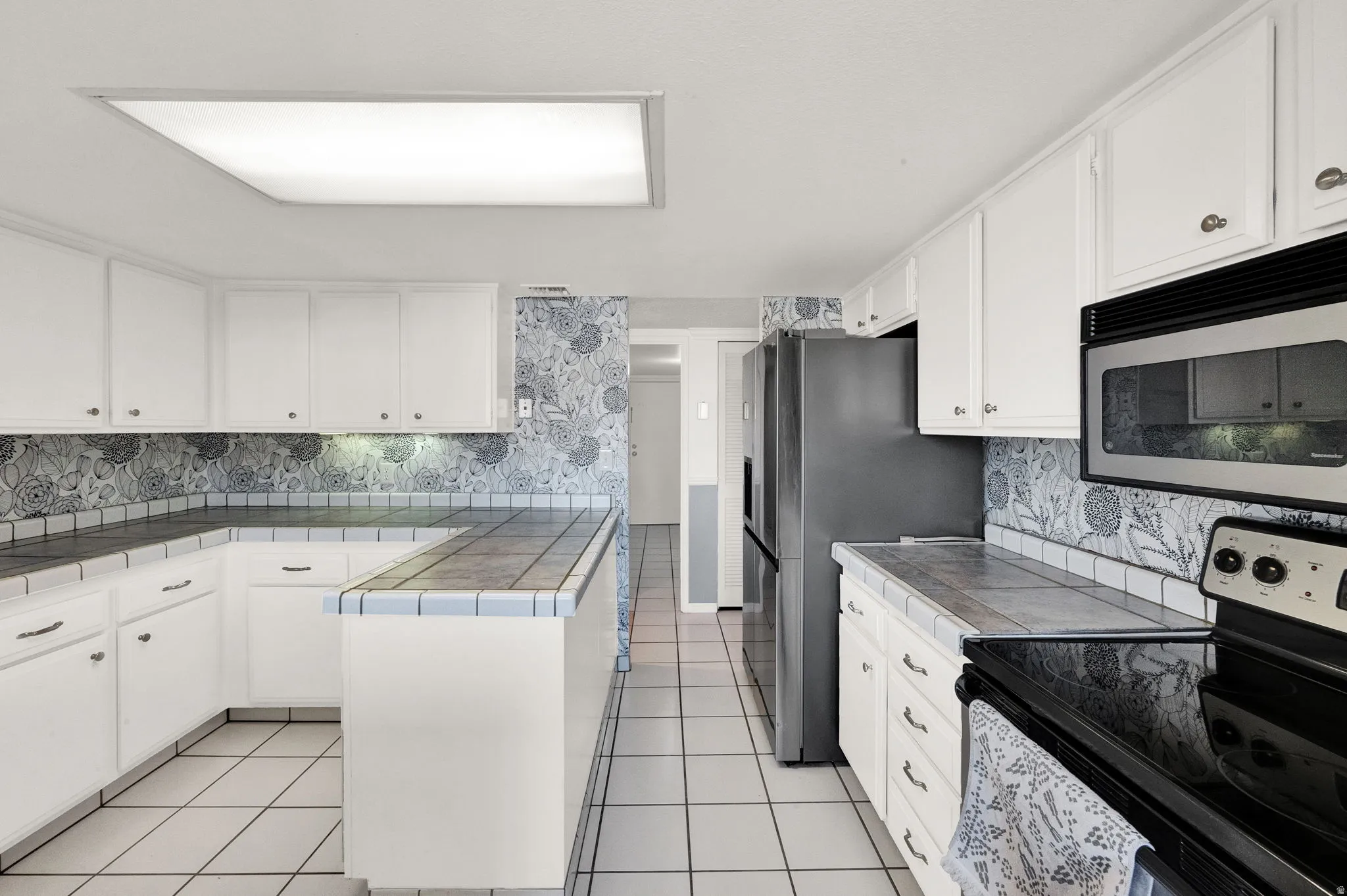 White cabinetry with dark hardware, tile flooring, built-in microwave, dark countertop, and stainless steel refrigerator