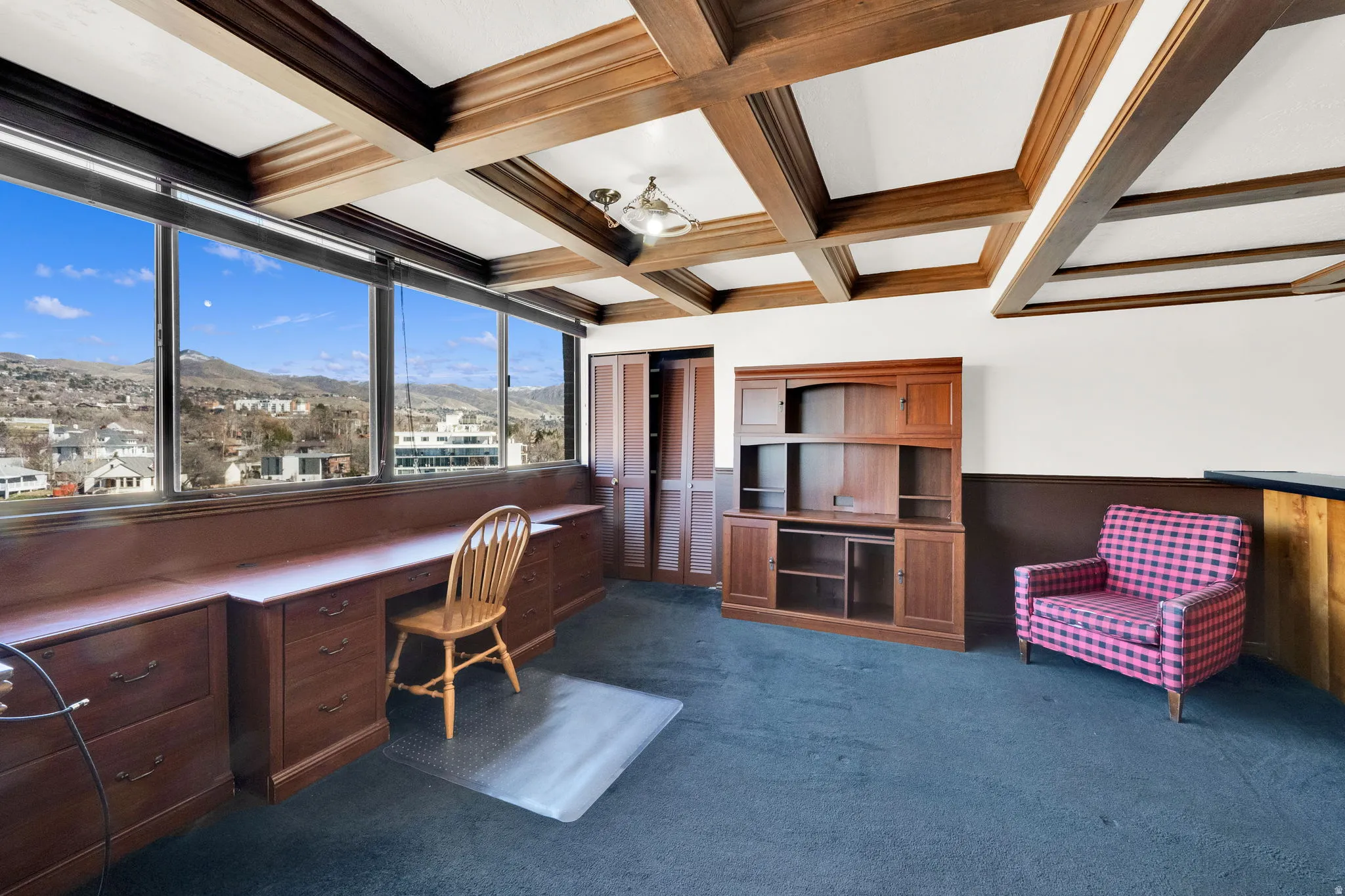 Wood-beam coffered ceiling, expansive windows, built-in wooden desk, rich wood-finish wainscoting, and recessed wood cabinetry