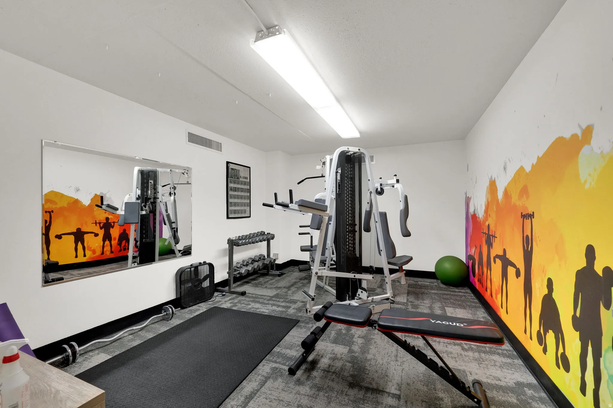 Dedicated fitness space featuring a full-wall mural, wall-mounted mirror, and recessed lighting