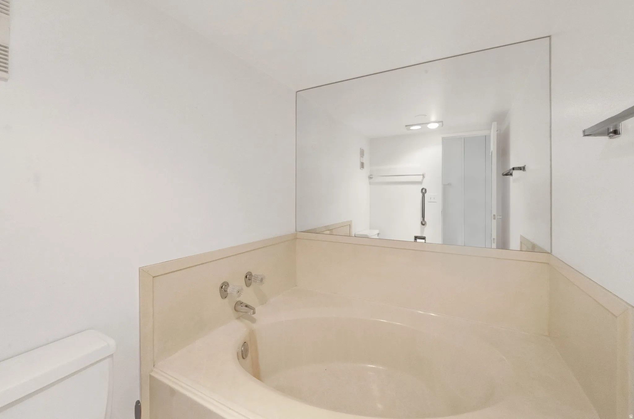 Built-in corner bathtub with deck-mounted fixtures, full-wall vanity mirror, and white wall finishes