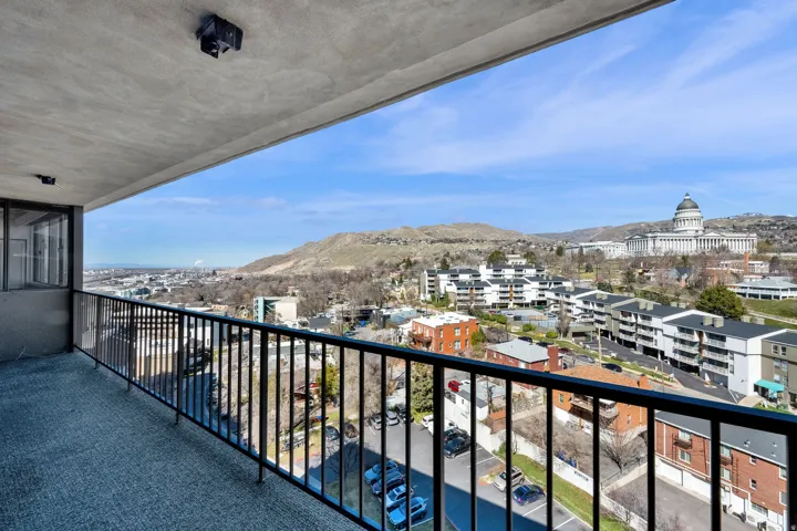 Balcony with black metal railing, concrete flooring, and an expansive skyline with distant architectural and natural elements