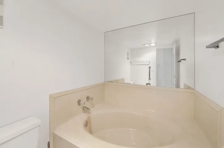 Built-in corner bathtub with deck-mounted fixtures, full-wall vanity mirror, and white wall finishes