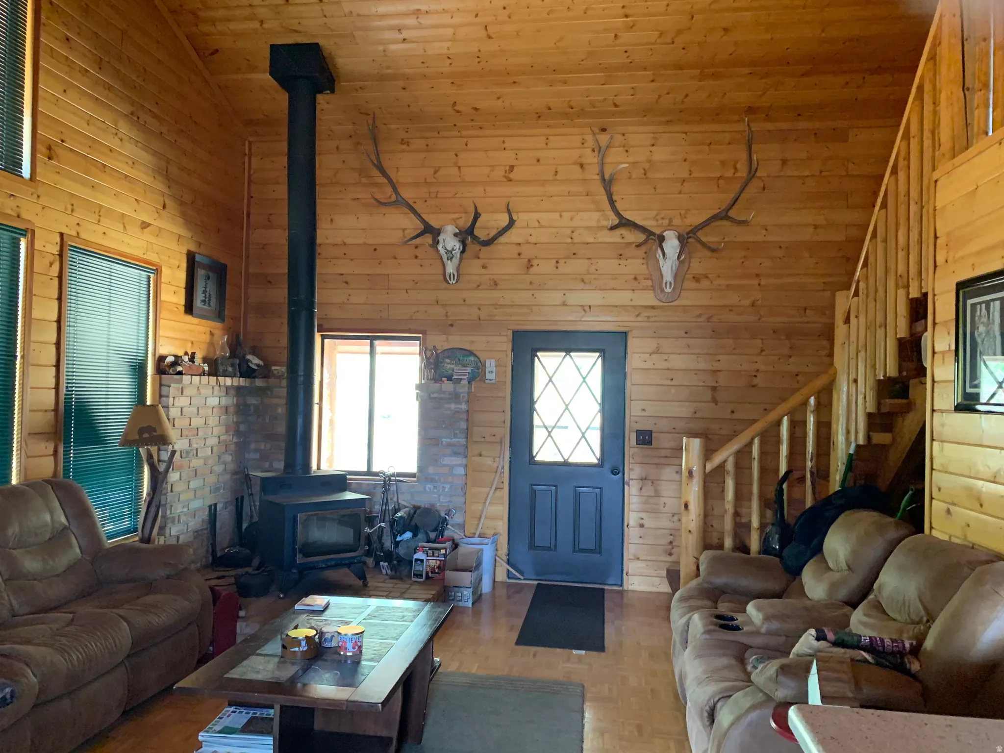 Wood-paneled interior walls, brick fireplace with a wood-burning stove, exposed wood ceiling beams, and a wood staircase with balusters