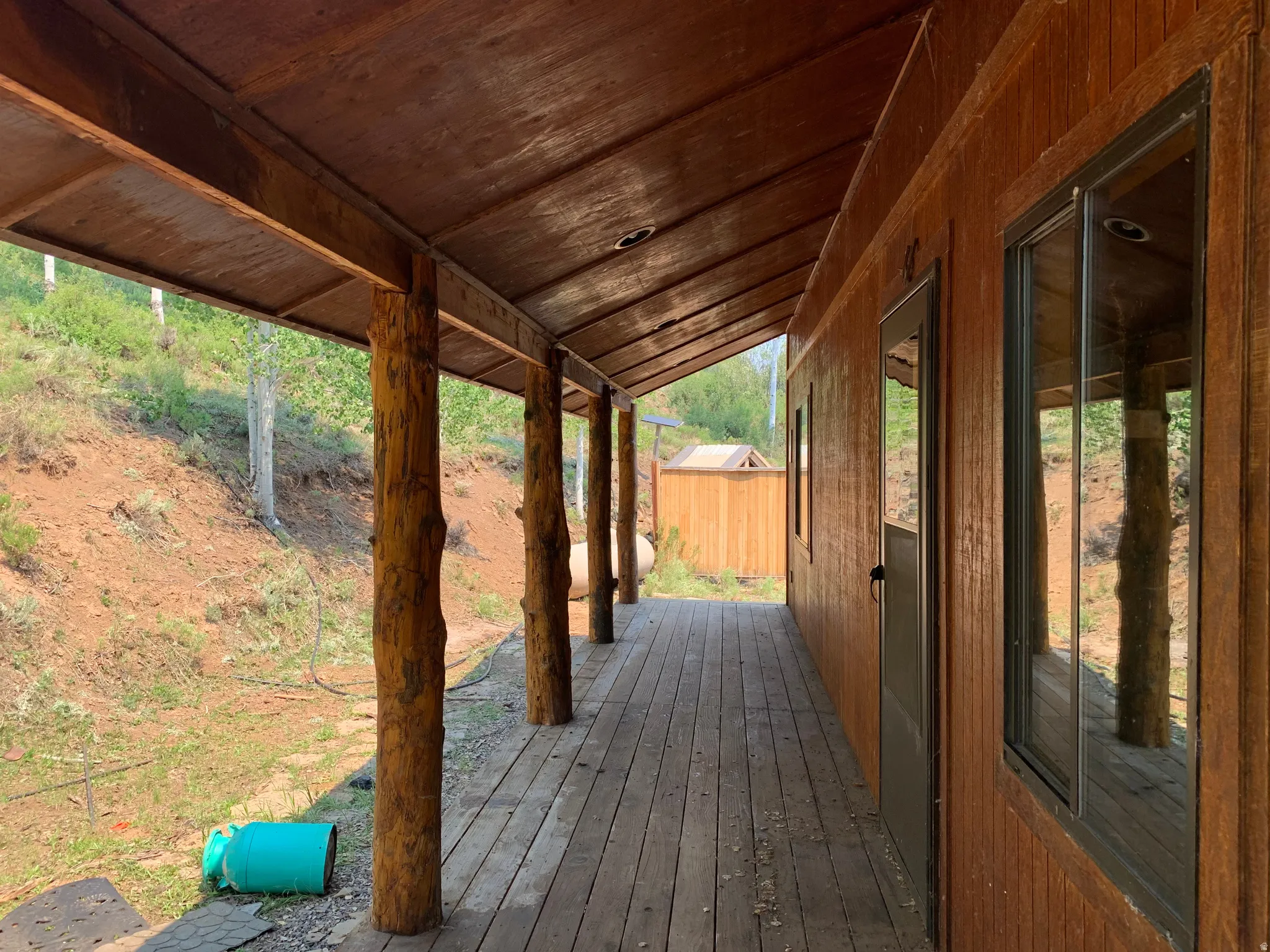 Covered porch with wood-plank flooring, natural log supports, and wood-paneled walls