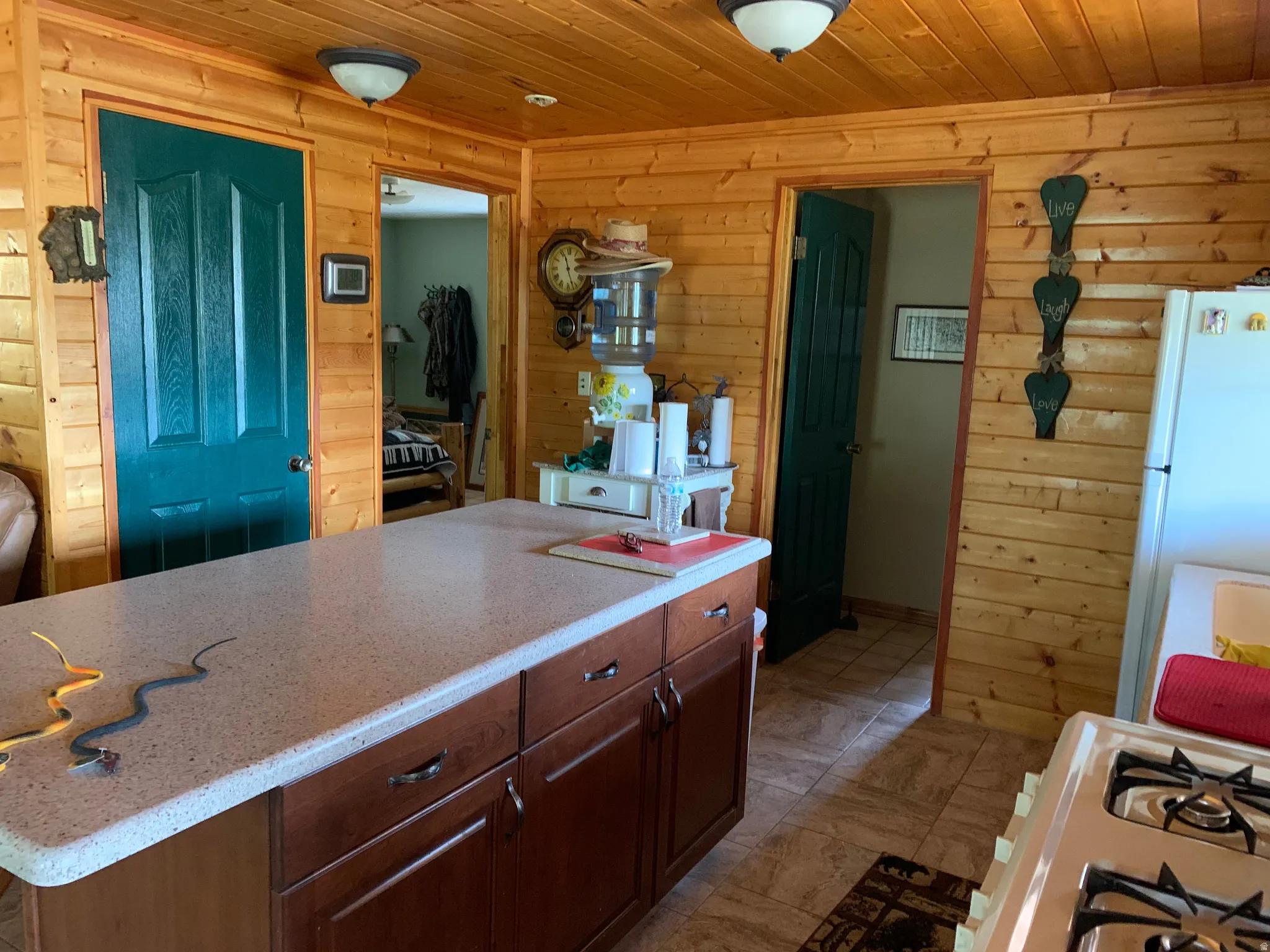 Wood-paneled walls and ceiling, center island with light-toned countertop, dark wood-finish cabinetry, and tile flooring