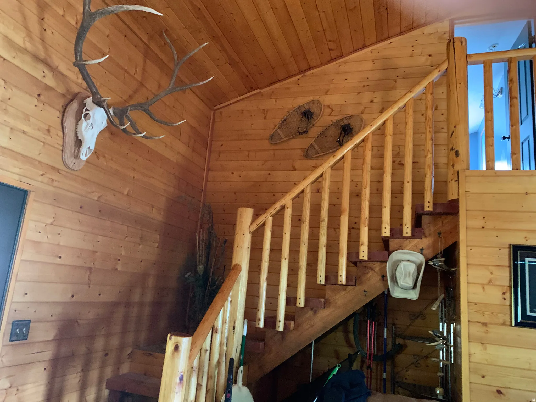 Wood-paneled walls and ceiling, custom wood staircase with log newel posts and spindles, wood-finish flooring