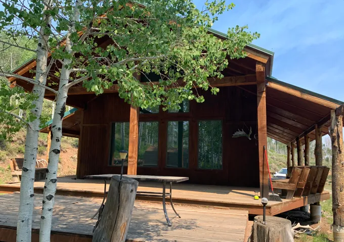 Expansive wood deck with a covered porch, large windows, wood siding, and robust log columns