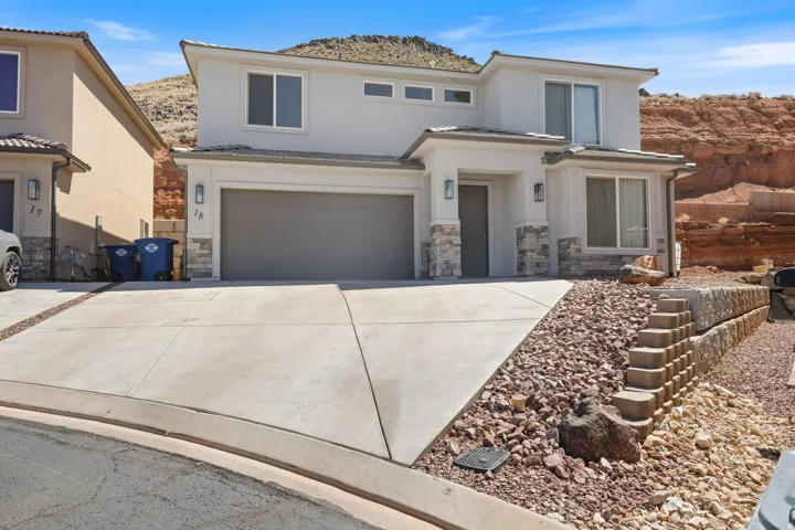 Contemporary stucco exterior with stone accents, a two-car garage, concrete driveway, and permanent outdoor lighting