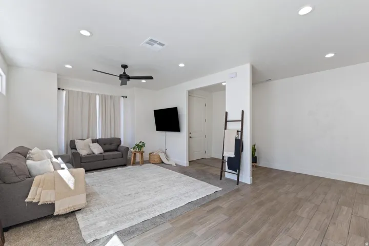 Recessed ceiling lighting, a modern ceiling fan, and wood-finish flooring