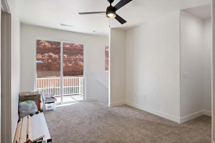 Neutral-toned carpeting, white walls, ceiling fan, sliding glass door, and a private balcony with white railing