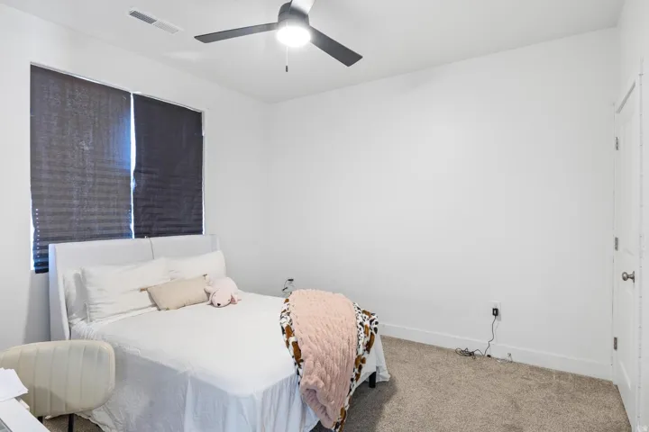 Recessed ceiling lighting, ceiling fan, window with roller shades, light-colored carpeting, and a white door