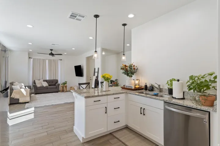 White cabinetry with dark hardware, stainless steel dishwasher, granite countertops, and wood-finish flooring