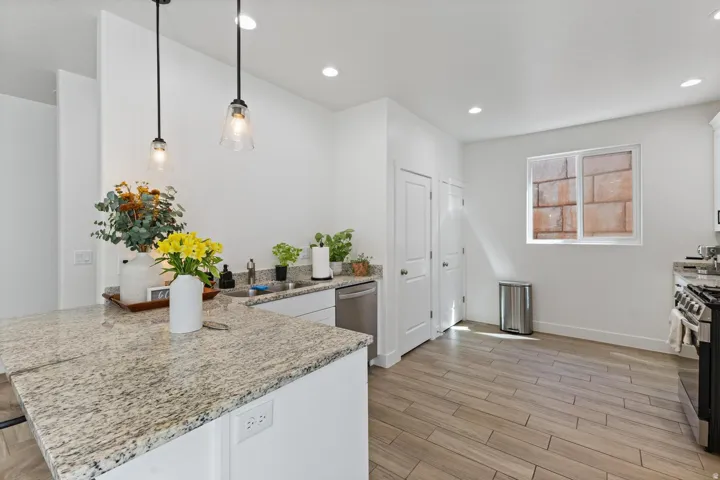 Kitchen featuring a granite-style island, pendant lighting, wood-finish flooring, recessed lighting, and white cabinetry