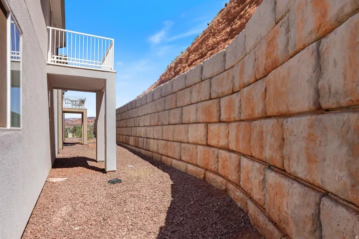 Stucco exterior, upper-level balcony with white railing, covered patio area, and a stone retaining wall