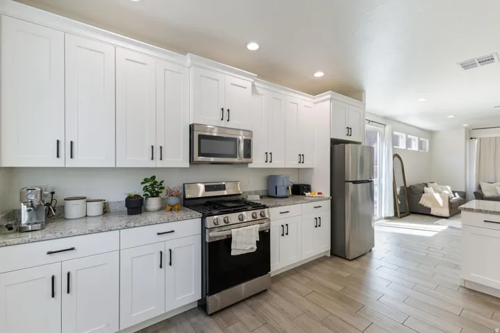 Kitchen featuring white shaker cabinetry, stainless steel appliances, speckled countertops, and wood-finish flooring