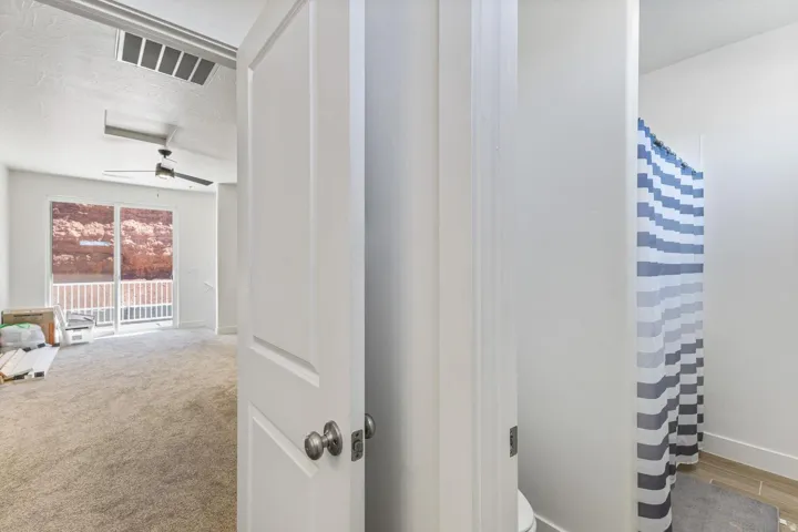 Spacious room with plush carpeting, ceiling fan, and sliding glass door leading to an outdoor balcony with white railing