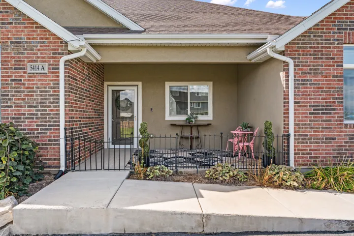 Brick exterior with covered entry, concrete walkway, and decorative metal fencing