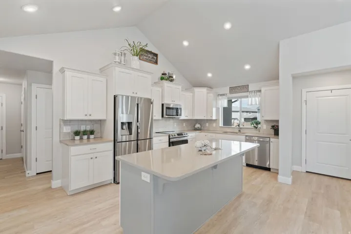 Kitchen featuring vaulted ceilings, recessed lighting, wood-finish flooring, white cabinetry, and stainless steel appliances