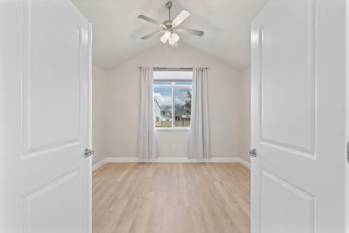 Vaulted ceiling with a ceiling fan, light wood-finish flooring, and a large window with white trim