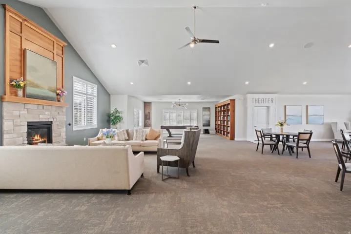 Community Clubhouse common area featuring a stone-clad fireplace with a wood mantel, vaulted ceiling with recessed lighting and a ceiling fan, and built-in wood shelving