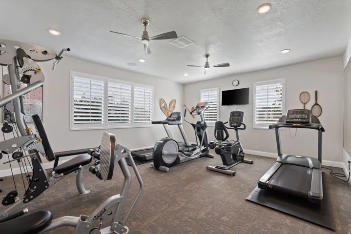 Recessed lighting, two ceiling fans, multiple windows with white plantation shutters, and light-toned wall paint