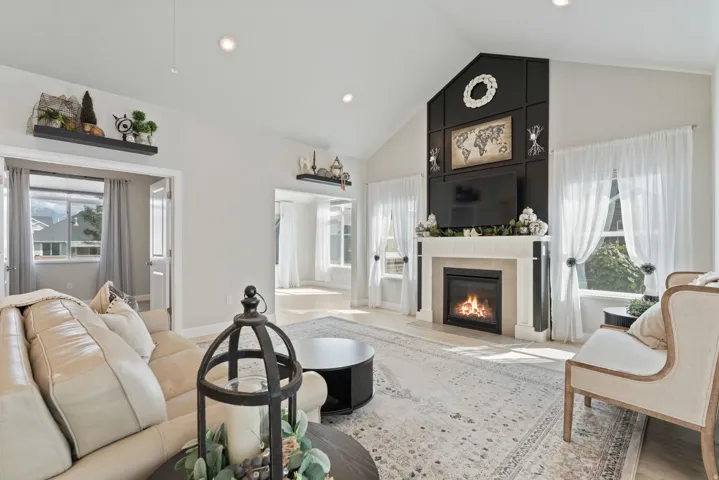 Vaulted ceiling with recessed lighting, fireplace with a stone-finish mantel, dark paneled accent wall, light wood-finish flooring, and multiple windows