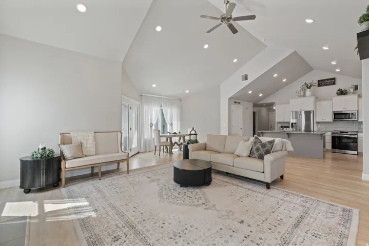 Vaulted ceilings with recessed lighting, wood-finish flooring, white shaker cabinetry, stainless steel appliances, and a ceiling fan