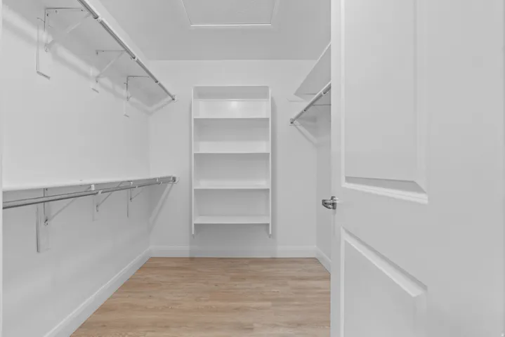 Walk-in closet featuring wood-finish flooring, built-in shelving, and multiple hanging rods