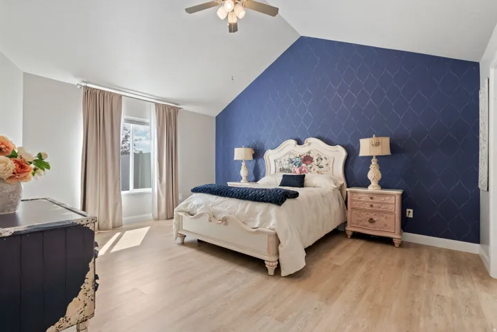 Vaulted ceiling with a ceiling fan, light wood-finish flooring, accent wall with geometric pattern, and a window with natural light