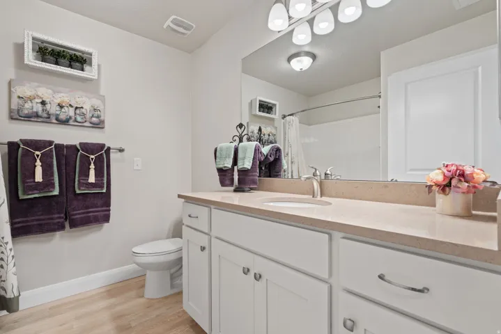 White vanity with panel cabinetry and silver hardware, under-mount sink, light-toned countertop, large wall mirror, and wood-finish flooring