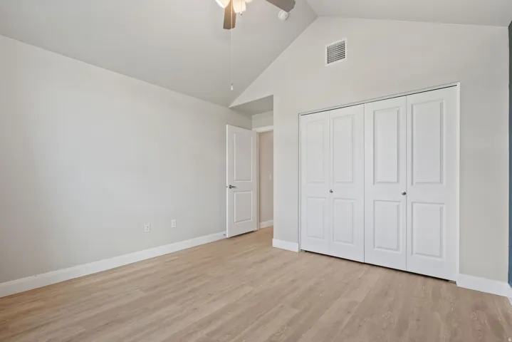 Vaulted ceiling with a ceiling fan, light wood-finish flooring, white bi-fold closet doors, and light neutral wall paint
