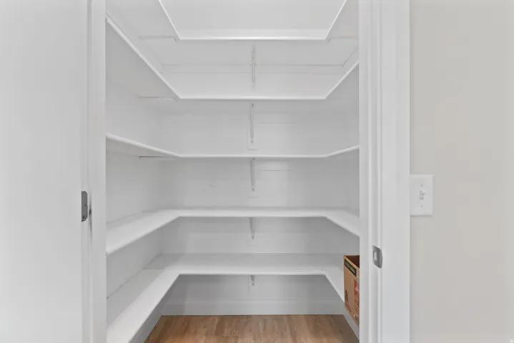 Walk-in pantry featuring multiple levels of white shelving and wood-finish flooring