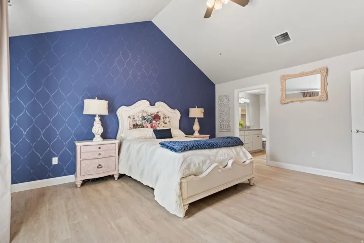 Vaulted ceiling with a ceiling fan, accent wall with patterned wallpaper, wood-finish flooring, and white interior doors