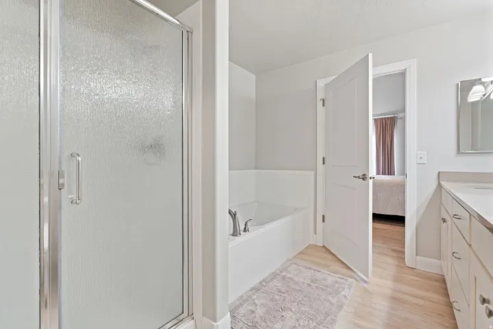 Frosted glass shower enclosure, built-in soaking tub, wood-finish flooring, and a vanity with dual sinks