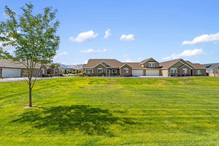 Expansive green lawn with mature tree, brick and siding exterior, multiple garage doors, and a multi-level roofline