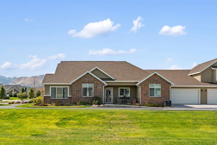 Brick and stucco exterior, prominent attached two-car garage, pitched shingle roof, paved driveway, and established front landscaping