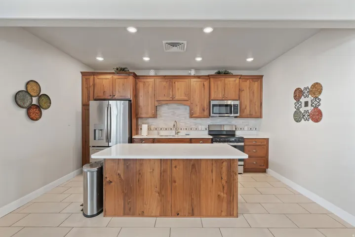 Kitchen featuring wood cabinetry, stainless steel appliances, a center island with a light-toned countertop, a tile backsplash, and recessed lighting