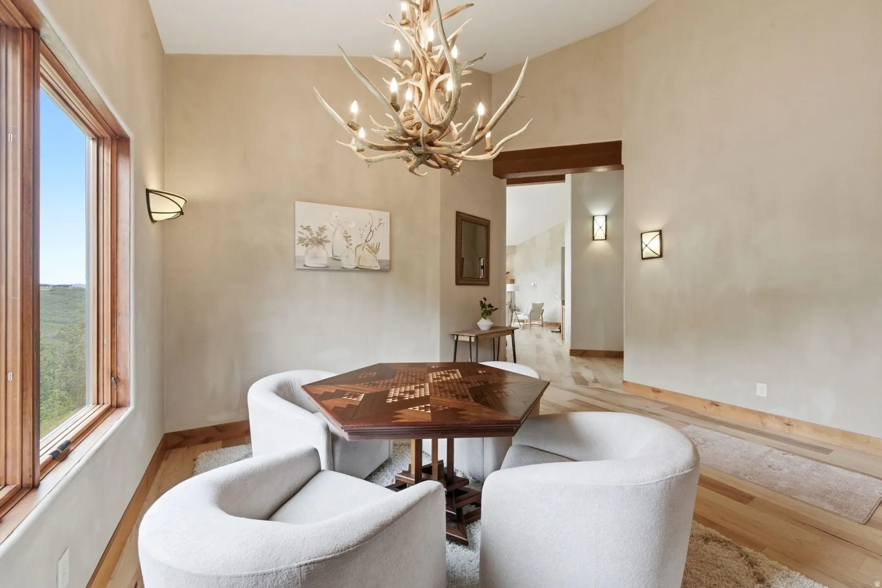 Large window with wood-frame trim, plaster walls, wood-finish flooring, and antler chandelier