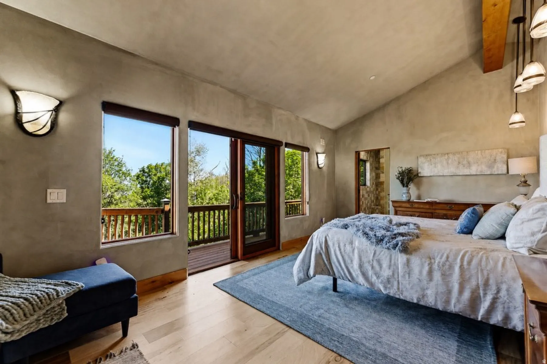 Vaulted ceiling with exposed wood beam, wood-finish flooring, built-in wall sconces, and a private balcony with wood railings