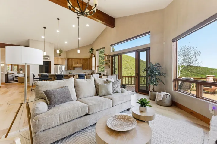 Vaulted ceilings with exposed beams, wood-finish flooring, large windows, sliding glass doors, and recessed lighting