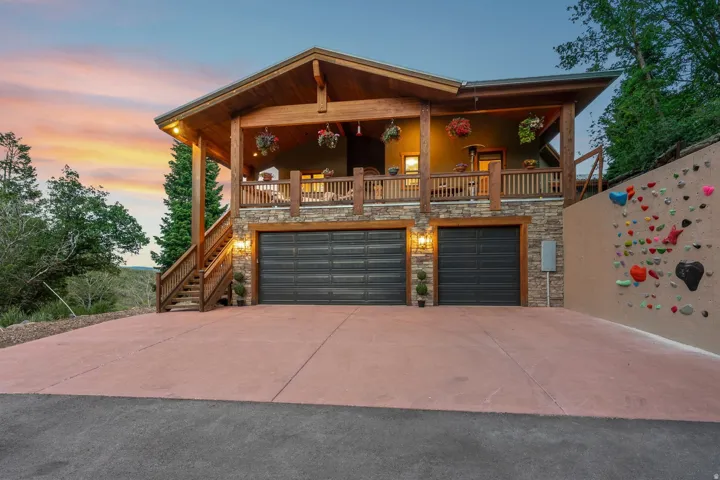 Stacked stone facade with two garage bays, a spacious upper deck featuring a wood railing, and a private climbing wall