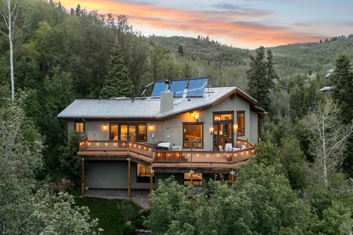 Multi-level residence featuring a corrugated metal roof, extensive decking with wood railings, and solar panels